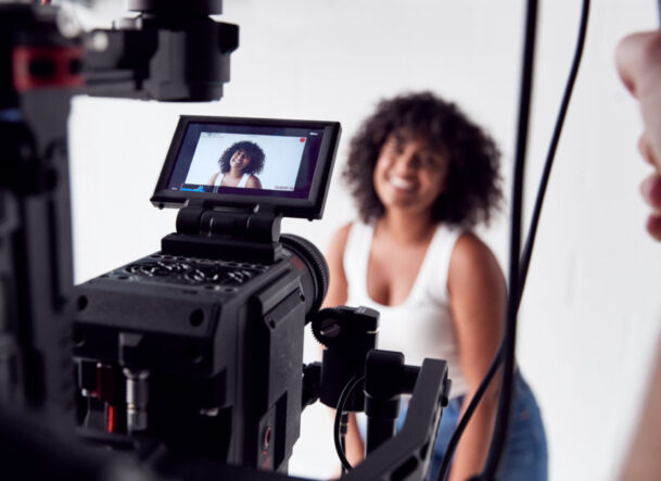 Portrait Of Smiling Casually Dressed Woman In Vest Top Standing Against White Brick Studio Wall
